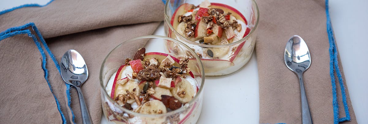 2 glass ramekins containing yoghurt topped with fruit and 2 spoons