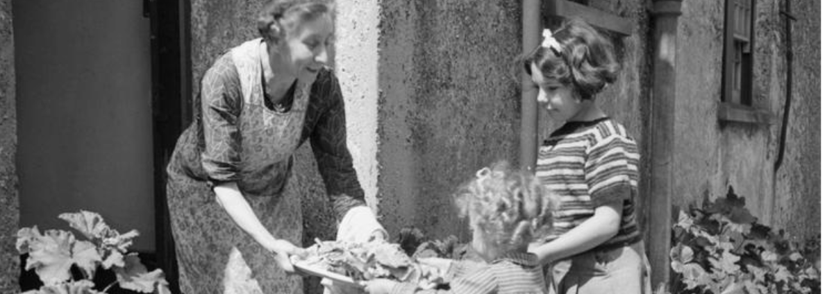 An image of two children and a woman in the 1950's holding a box containing food waste.